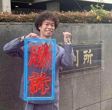 　手作りの「勝訴」ボードを手にガッツポーズする渡邊センス