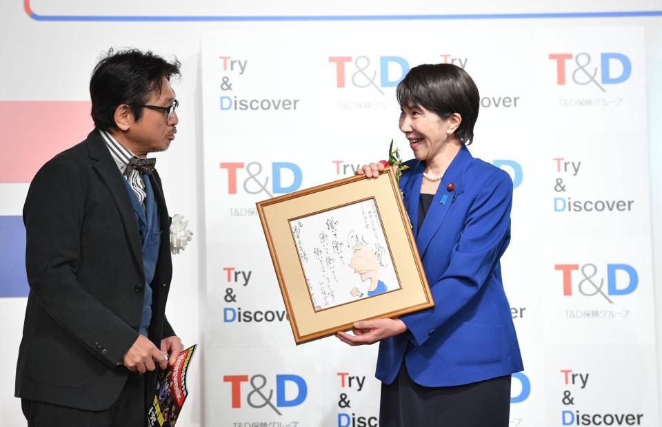　選考委員のやくみつる（左）からイラスト入り色紙をプレゼントされ感激の高市早苗首相（撮影・開出牧）
