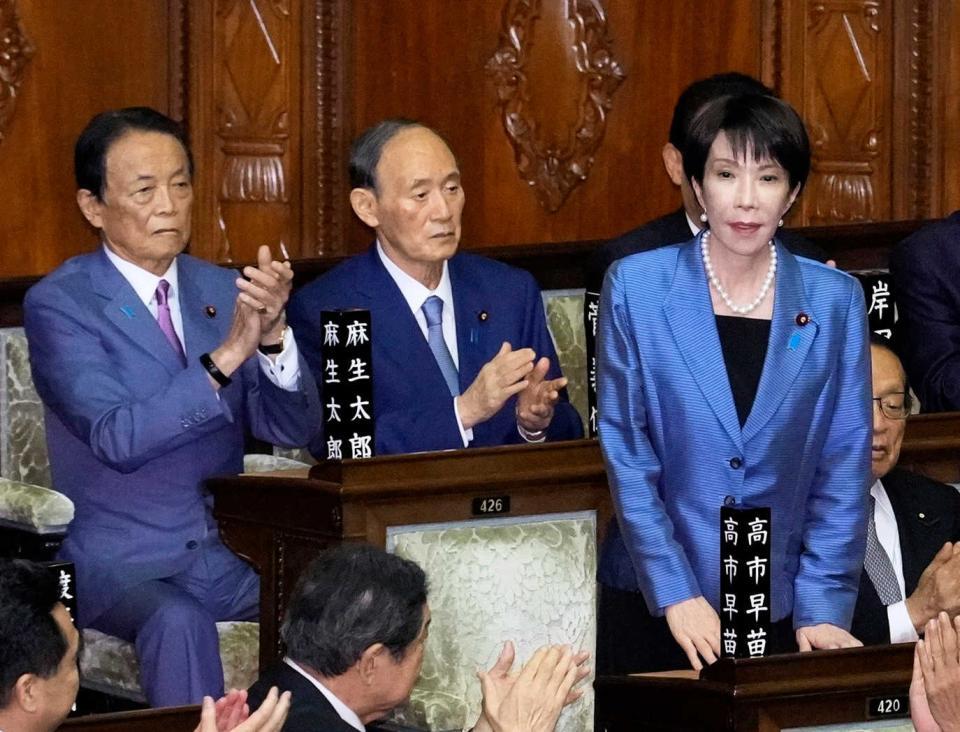 　衆院本会議で第１０４代首相に指名され、起立する自民党の高市早苗総裁。後方が麻生太郎氏と菅義偉氏＝２０２５年１０月