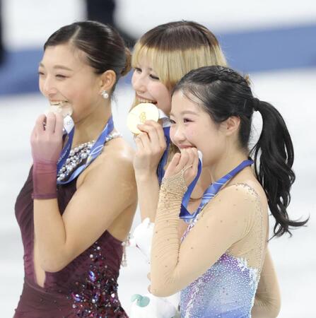 ミラノ・コルティナ五輪メダルをかじる（手前から）中井亜美、アリサ・リュウ、坂本花織＝ミラノアイススケートアリーナ（撮影・吉澤敬太）