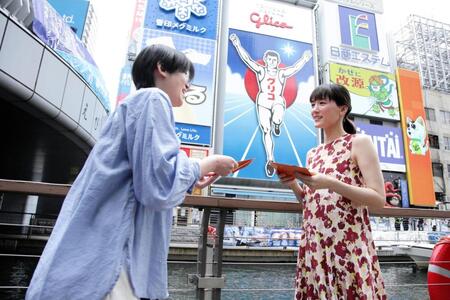 道頓堀グリコサイン前で、道行く人にラブレターを手渡しする綾瀬はるか（右）　©２０２６　映画「人はなぜラブレターを書くのか」製作委員会