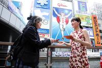 道頓堀グリコサイン前で、道行く人にラブレターを手渡しする綾瀬はるか（右）　©２０２６　映画「人はなぜラブレターを書くのか」製作委員会