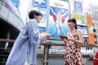 道頓堀グリコサイン前で、道行く人にラブレターを手渡しする綾瀬はるか（右）　©２０２６　映画「人はなぜラブレターを書くのか」製作委員会