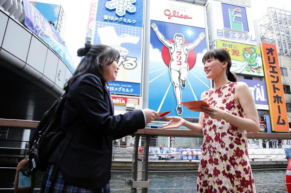 道頓堀グリコサイン前で、道行く人にラブレターを手渡しする綾瀬はるか（右）　©２０２６　映画「人はなぜラブレターを書くのか」製作委員会
