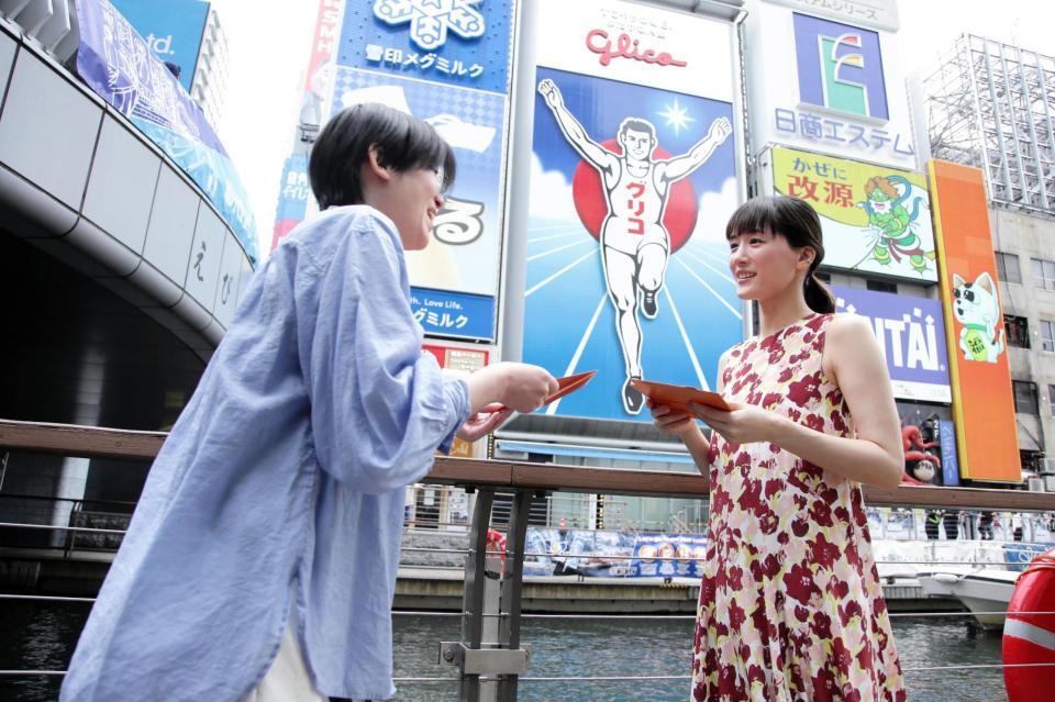 道頓堀グリコサイン前で、道行く人にラブレターを手渡しする綾瀬はるか（右）　©２０２６　映画「人はなぜラブレターを書くのか」製作委員会