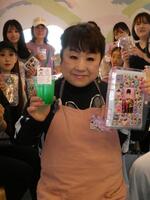 シール帳を掲げる天童よしみ、（後ろの）来店客＝東京・しぇあぷく原宿店