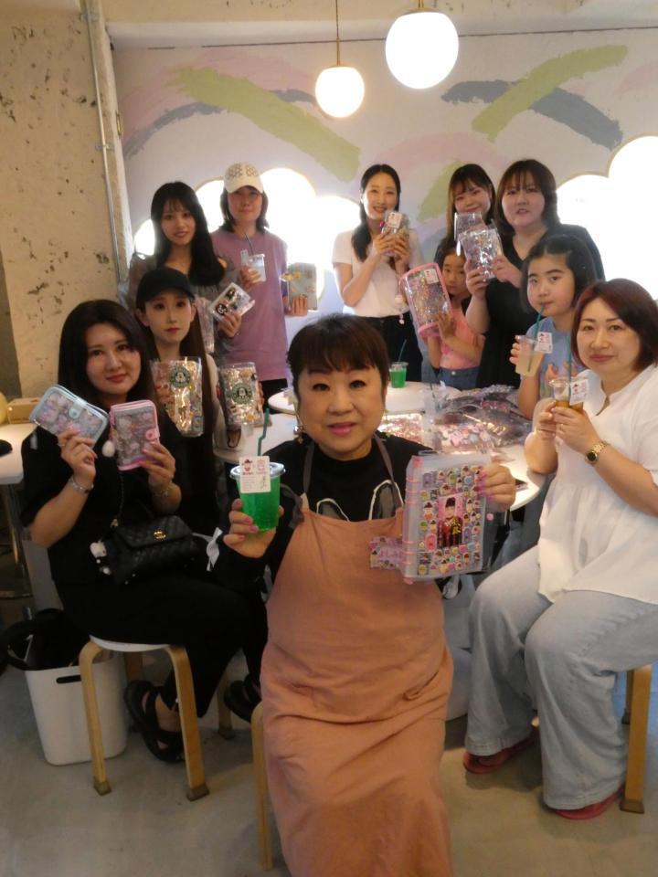 シール帳を掲げる天童よしみ、（後ろの）来店客＝東京・しぇあぷく原宿店