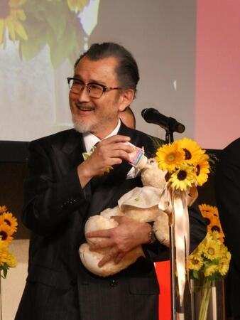 赤ちゃんの重さがあるぬいぐるみを抱え、育児用ミルクをあげるポーズをとる吉田鋼太郎＝都内