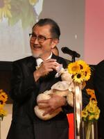 赤ちゃんの重さがあるぬいぐるみを抱え、育児用ミルクをあげるポーズをとる吉田鋼太郎＝都内