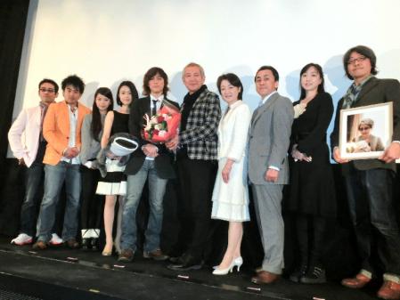 馬渕晴子さんの遺影を持つ矢城潤一監督（右）と、舞台あいさつに登場した（左から）大城英司プロデューサー、今井ゆうぞう、趣里、原田佳奈、塩谷瞬、中原丈雄、黒田福美、佐藤Ｂ作、川上麻衣子＝東京・銀座シネパトス