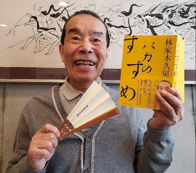 事務所に掲げた絵の師匠・清水崑さんの作品前で、著書「バカのすすめ」を手にする林家木久扇。８５歳の記念落語会を開催する＝都内