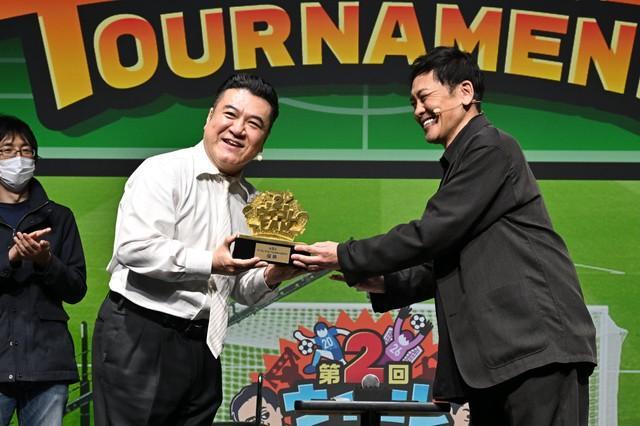 リアルイベント「ウイコレ FAN TOURNAMENT」で連覇を達成し、有田哲平（右）から優勝トロフィーを受け取る山崎弘也