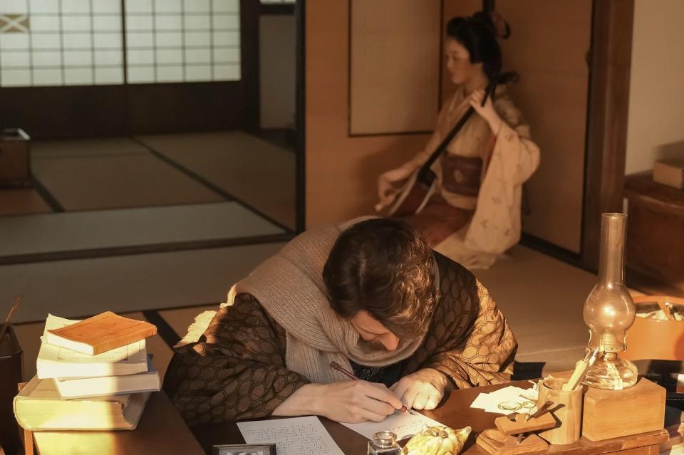 机に向かうヘブン（トミー・バストウ）の後ろで三味線を奏でるトキ（高石あかり）