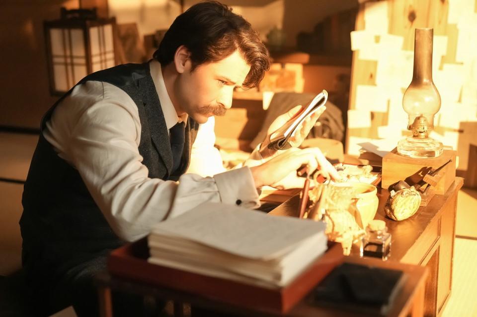 真剣な面持ちで机に向かうヘブン（トミー・バストウ）