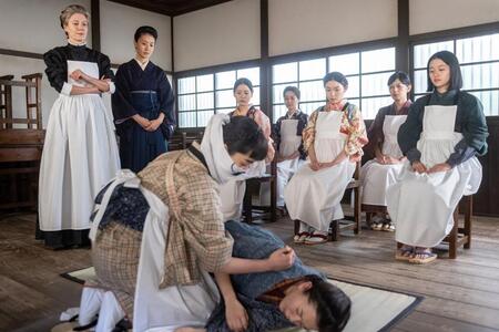バーンズ先生（エマ・ハワード・左）のもと、りん（見上愛・前列左）や直美（上坂樹里・後列右）たちはコレラ感染者を看護する模擬授業に取り組む