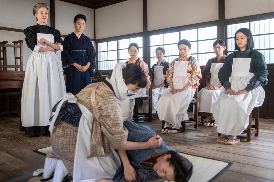 バーンズ先生（エマ・ハワード・左）のもと、りん（見上愛・前列左）や直美（上坂樹里・後列右）たちはコレラ感染者を看護する模擬授業に取り組む