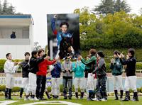 　亡くなった後藤騎手のパネルを高く掲げるジョッキー仲間たち