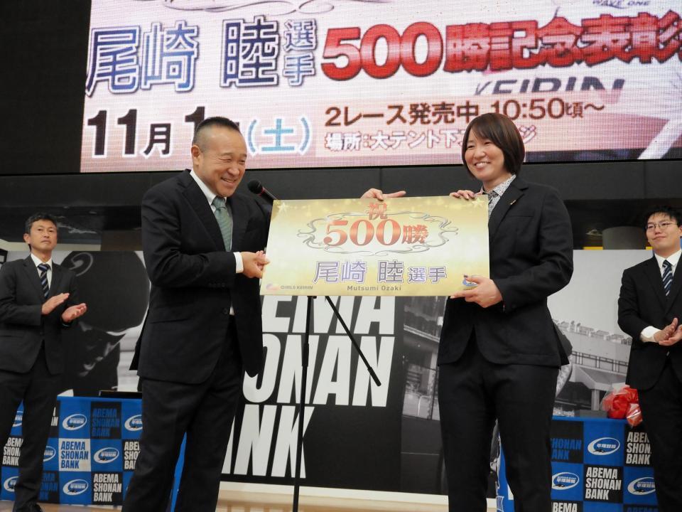 　５００勝記念パネルを高木隆弘支部長（左）からもらう尾崎睦