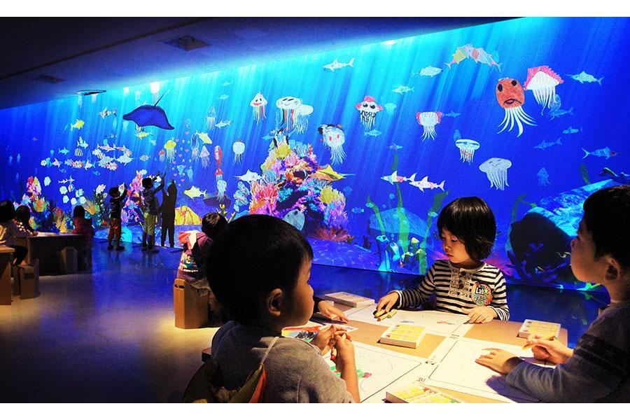 　子どもの描いた色とりどりの海の生物が泳ぎ回る、巨大な水槽を模したスクリーン