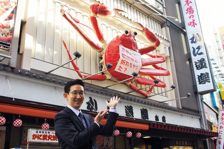 　１０月２３日まで修理のため脚が２本なくなった「かに道楽」の名物看板と小林泰三店長（１０月２０日・大阪市中央区）