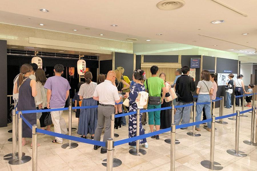 　「甦る!!令和の比叡山お化け屋敷」に並ぶ来場者。会場前の大きな看板で記念撮影する姿も多いそう（京都市下京区・大丸京都店）