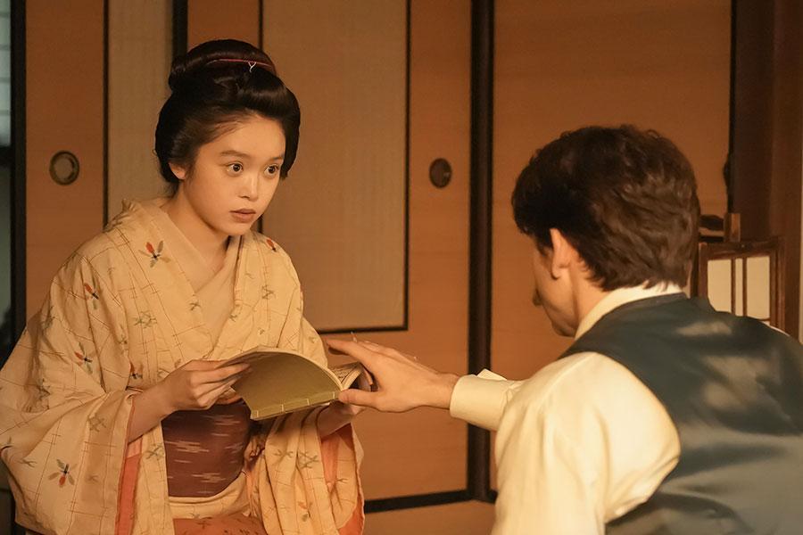 　『ばけばけ』第５７回より。『本邦諸国奇談集』を手に取るトキ（高石あかり）を制するヘブン（トミー･バストウ）©ＮＨＫ