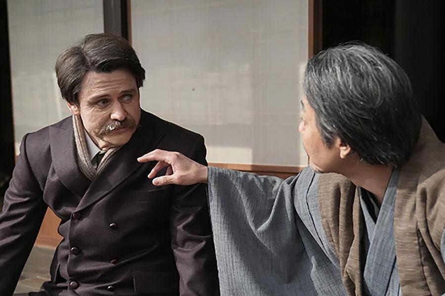 　『ばけばけ』第１１６回より。縁側でヘブン（写真左、トミー･バストウ）と話すトキの父・司之介（写真右、岡部たかし）©ＮＨＫ