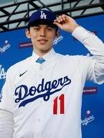 ドジャースの入団記者会見で、背番号１１のユニホームに袖を通し撮影に応じる佐々木（共同）