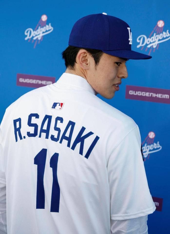 ドジャースの入団記者会見で背番号１１のユニホームに袖を通し、撮影に応じる佐々木（共同）