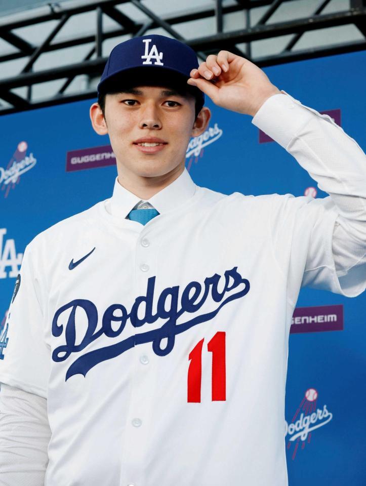 　ドジャースの入団会見で、背番号１１のユニホームに袖を通す佐々木（共同）