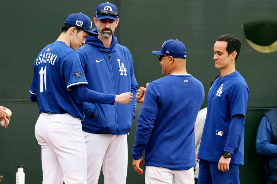 　ブルペンで投球練習後、ロバーツ監督（右から２人目）とタッチを交わす佐々木。奥はプライアー投手コーチ