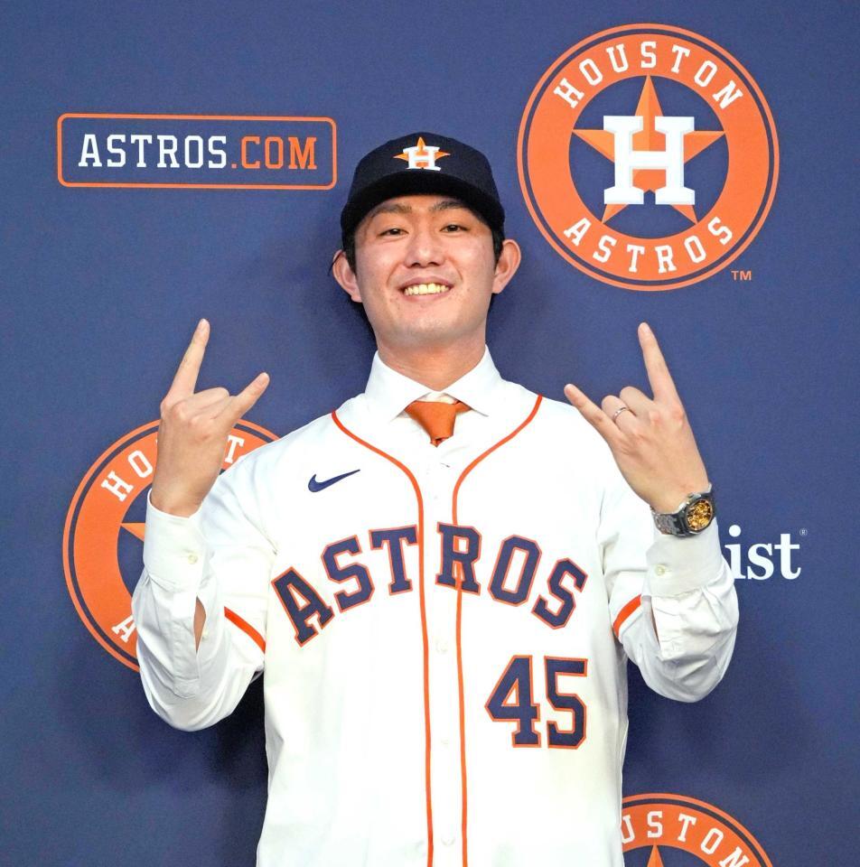 　アストロズの入団会見でユニホームに袖を通し、ポーズをとる今井（共同）