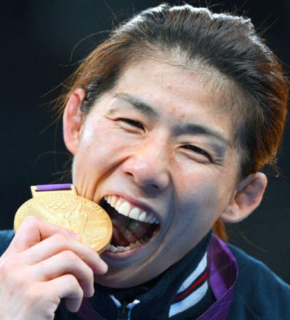 女子５５キロ級で獲得した金メダルをかじってみせる吉田沙保里（共同）