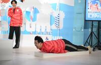 スケルトンブース体験に挑戦するレインボーのジャンボたかお。後方は池田直人（撮影・開出牧）