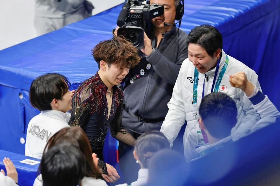 団体男子フリーの演技を終え、鍵山優真（左）や日下匡力コーチ（右）らに迎えられる佐藤駿＝ミラノ（共同）