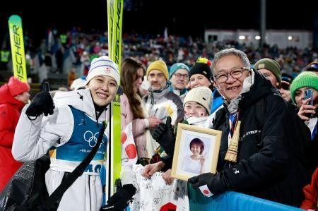 　女子個人ラージヒルを終え、母信子さんの写真を持つ父守さん（右）と撮影に応じる丸山希＝プレダッツォ（共同）