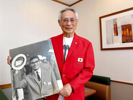 　６４年東京五輪の赤ブレザーを着用し、閉会式での自身の写真を手にする鈴木章介さん＝１９年６月