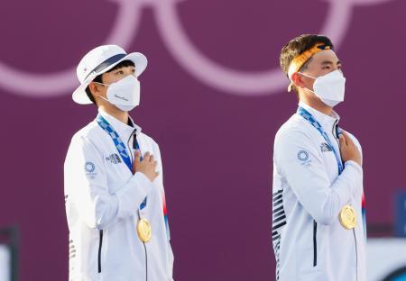 　混合団体で金メダルを獲得し、表彰式で国旗を見つめる韓国の安山（左）と金済徳＝２４日、夢の島公園アーチェリー場