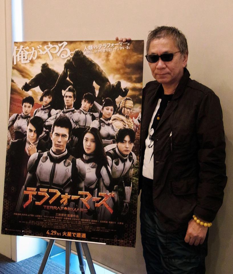 ポスターと並ぶ三池崇史監督＝都内