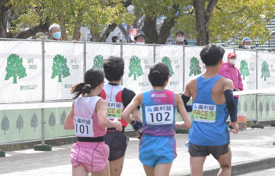 周回コースと公園を仕切ったフェンスの上から、レースの様子をのぞき込む人々＝１月31日、長居公園（撮影・高部洋祐）