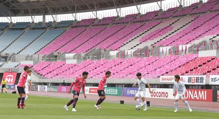 空席に置かれたピンクのポンチョを背に戦う両チームの選手ら＝２日、ヤンマースタジアム長居（撮影・高部洋祐）