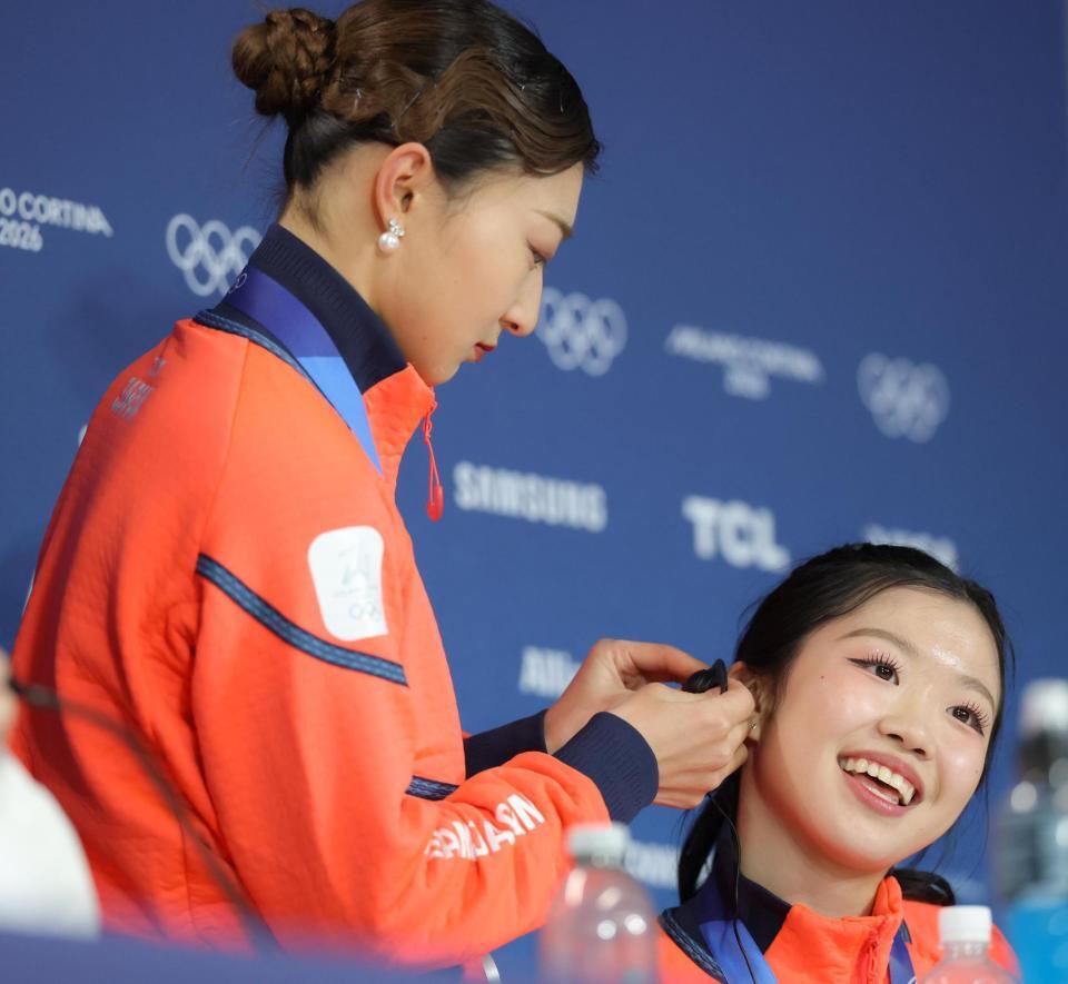 メダリスト会見時、同時通訳のイヤホンをうまくつけられない中井亜美（右）の耳に、つけてあげる坂本花織＝１９日、ミラノアイススケートアリーナ（撮影・吉澤敬太）