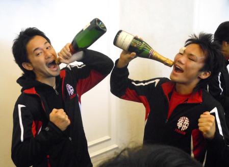 　洋酒の瓶を手に“勝利の美酒”を浴びるポーズをする山中慎介（左）と五十嵐俊幸