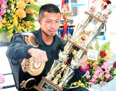 お祝いの花束に囲まれて拳を突き出す内山高志