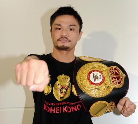 帰国した河野公平はチャンピオンベルトを担いでポーズを決める＝成田空港（撮影・開出牧）