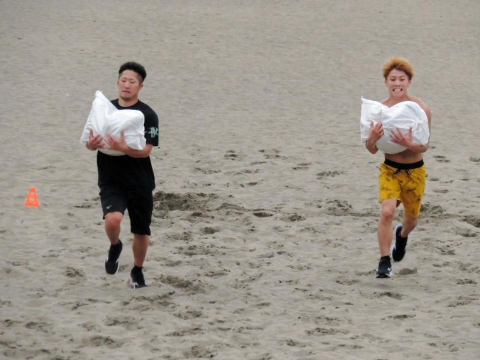 重さ１７キロの土のうを抱えて砂浜を走る井上拓真（左）と兄の尚弥＝静岡県熱海市