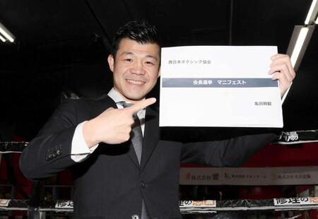 　マニフェストを手にポーズを決める亀田興毅氏（撮影・石井剣太郎）