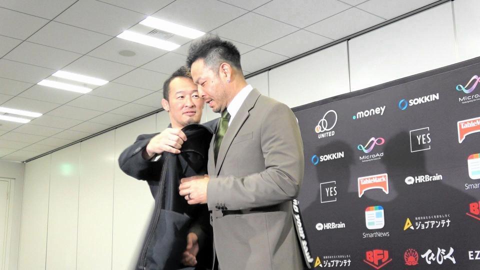 　写真撮影で強引にジャケットの上からジャージを着せようとする丸藤正道副社長（左）と、それをいやがるＫＥＮＴＡ