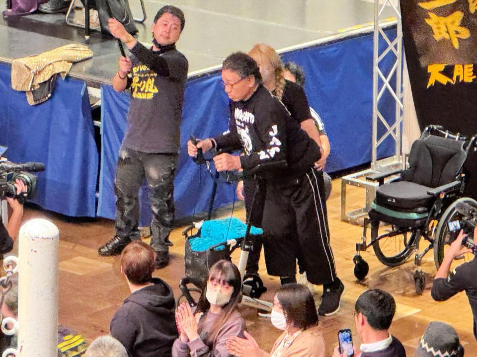 　娘の嶋田紋奈代表に支えられながら、車いすを降りて歩行器で自力歩行する姿を披露した天龍源一郎