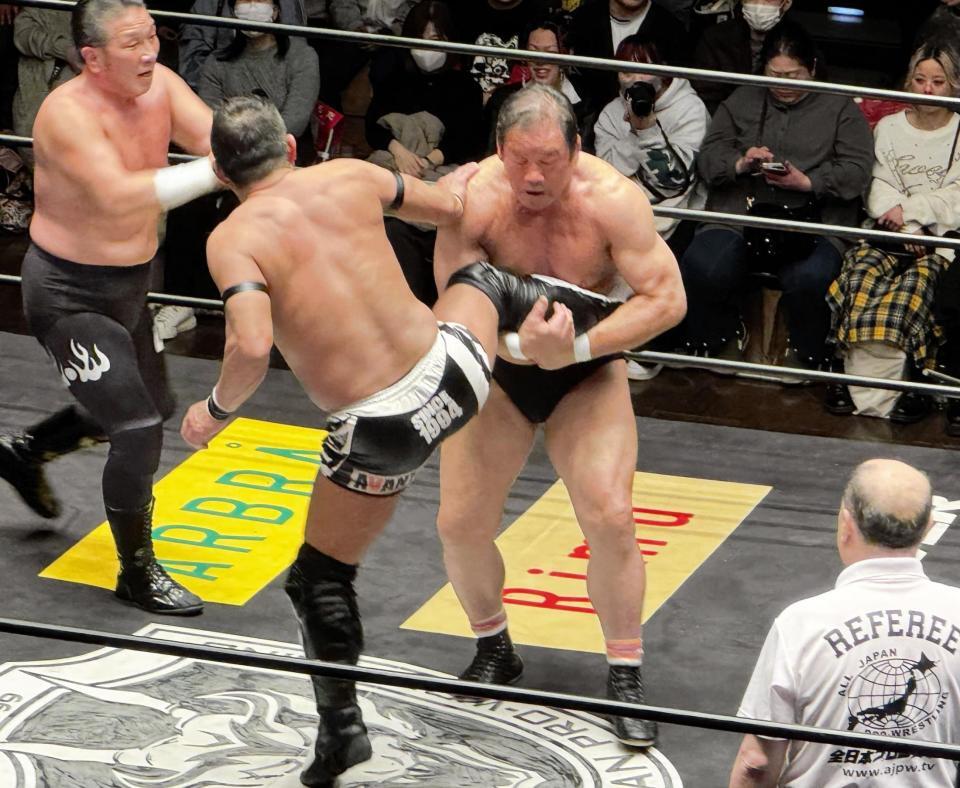 望月成晃（手前）のキックをキャッチし、ドラゴンスクリューを狙う藤波辰爾